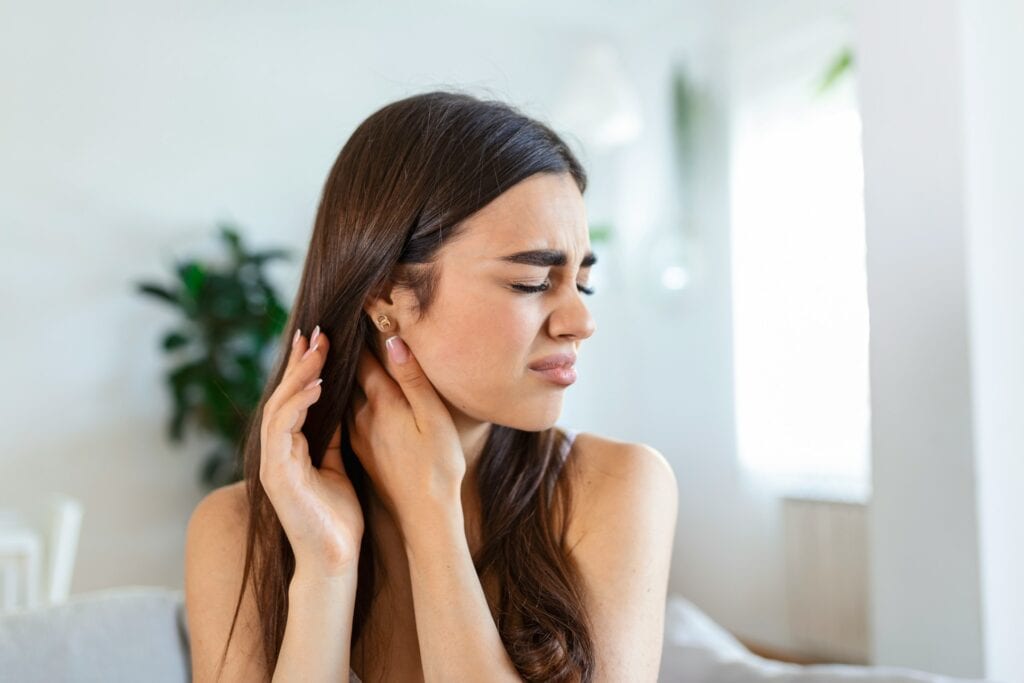Young woman with closed eyes pressing both hands against her ear