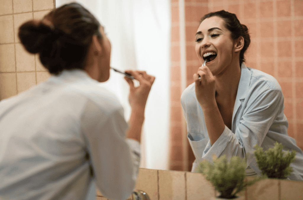 Woman brushing her teeth while looking at her reflection