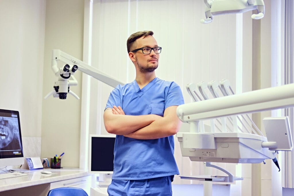Dentist standing with arms crossed in a dental clinic, with dental equipment
